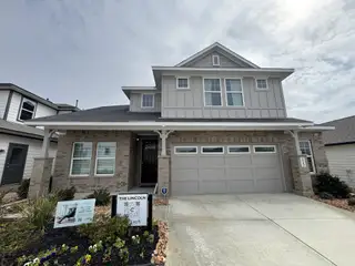 Street view A charming brick home with a welcoming porch and landscaped front yard in Hunters Ranch by Chesmar Homes (San Antonio, TX).