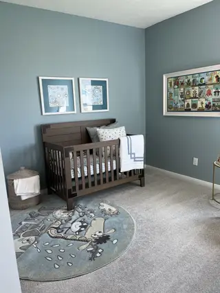 Charming nursery with a wooden crib, whimsical round rug, soft gray carpet, and playful art on blue walls.