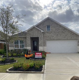 Street view A charming brick home with a well-kept yard in Cypress Green by Colina Homes (Hockley, TX).