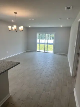Bright, open living area with sleek tile floors, modern chandelier, and sliding glass doors to a sunny backyard.