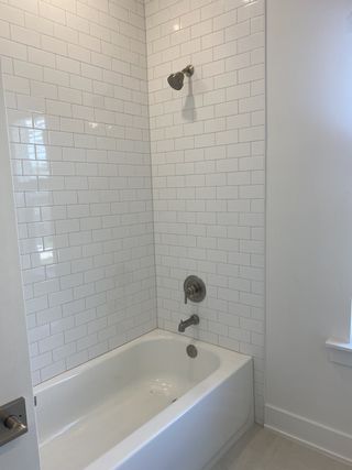 Model Home A sleek bathroom with a white tub and glossy subway tile, creating a fresh and clean atmosphere.