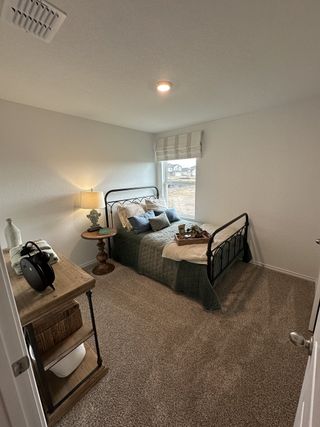 Cozy bedroom with plush carpet, a metal bedframe, soft lighting, and rustic wooden furniture for a welcoming feel.