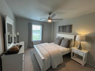 Model Home A cozy bedroom featuring a white bed, soft gray walls, and elegant décor with natural light from a large window.