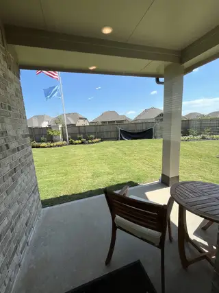 Model Home A cozy patio with chairs overlooking a lush green backyard under clear skies, perfect for relaxation and outdoor enjoyment.