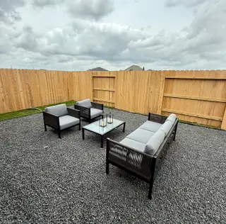 Model Home A minimalist outdoor space with sleek furniture, gravel flooring, and a wooden fence under a cloudy sky.