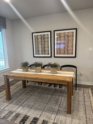 A cozy dining area with a wooden table, decorative wall art, and a textured rug, complemented by potted greenery.