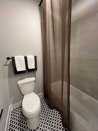 A modern bathroom with geometric floor tiles, a sleek white toilet, and a textured brown shower curtain.
