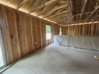 Model Home A framed interior under construction with exposed wooden beams and plastic-covered building materials on the floor.