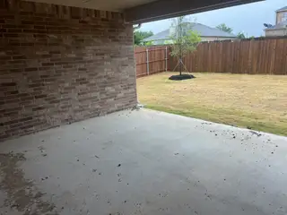 A covered patio with a brick wall and spacious fenced backyard, perfect for outdoor relaxation and gatherings.