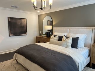 A sophisticated bedroom with a plush bed, elegant chandelier, and modern artwork.