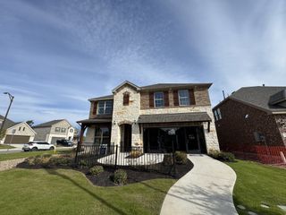 A charming stone and brick home with elegant shutters and a manicured lawn in Highland Village by Pulte Homes (Georgetown, TX).