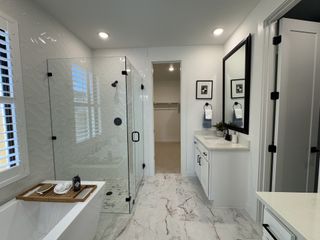 A modern bathroom featuring a glass shower, marble floor, and sleek vanity with stylish accents and art.