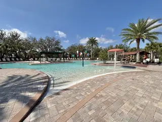 A resort-style pool with lounge chairs, palm trees, and a splash fountain in Kindred by D.R. Horton (Kissimmee, FL).