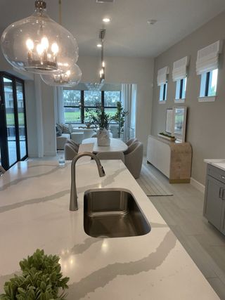 Model Home A modern kitchen-dining area featuring elegant lighting, a sleek marble island, and large windows with a lush outdoor view.