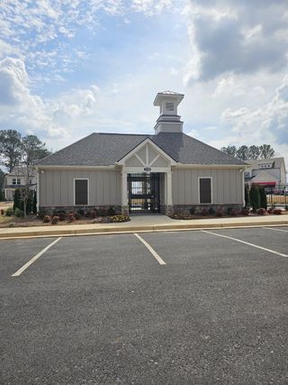  A charming clubhouse with light gray siding, a stone base, and a small tower stands prominently with a gated entrance and paved parking, in Bailey Fence by Taylor Morrison (Dacula, GA).