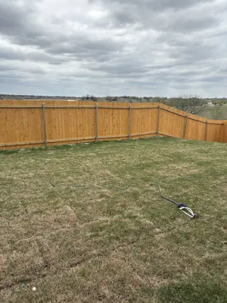 A spacious fenced backyard with lush greenery under a cloudy sky in Vista West by LGI Homes (Fort Worth, TX).