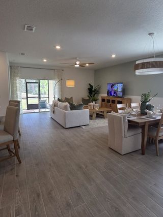 Open living space with wood flooring, cozy seating, and a dining area. Features a ceiling fan and natural lighting.