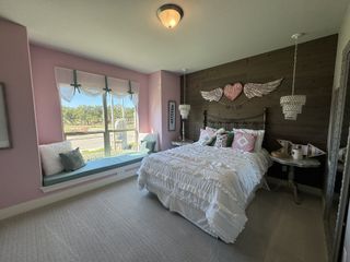 A charming bedroom featuring pink walls, a cozy window seat, ruffled bedding, and stylish pendant lighting.