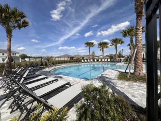 A sparkling community pool in Meadowlark Landing (Apopka, FL) by Mattamy Homes features lounge chairs, palm trees, and a bright blue sky above.