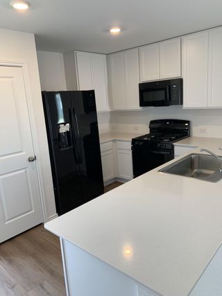 A contemporary kitchen featuring white cabinetry, black appliances, and a spacious quartz countertop island for dining and meal prep.