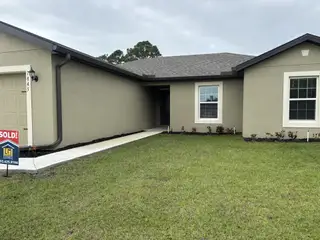 A charming beige home with inviting windows and manicured landscaping in Vero Lake Estates by LGI Homes (Vero Beach, FL).