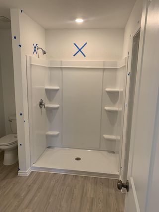 Model Home A modern bathroom featuring a spacious walk-in shower, white fixtures, and sleek wood flooring.