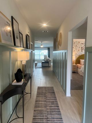 A sleek hallway with light wood flooring, decorative wainscoting, and a stylish console table adorned with art and a warm lamp.
