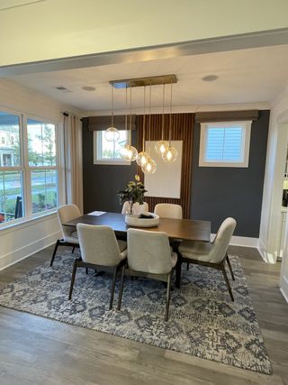 A modern dining room with elegant pendant lighting, a wooden table, upholstered chairs, and a patterned rug.