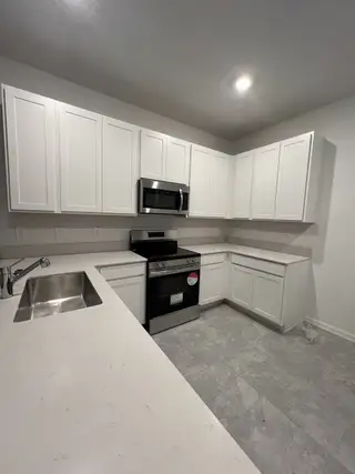 Model Home A modern kitchen featuring white cabinets, sleek countertops, stainless steel appliances, and gray tile flooring.