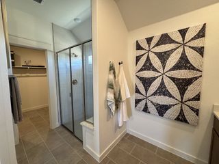 Model Home A modern bathroom with a glass shower, geometric wall art, and open closet space.