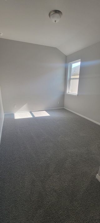 A bright, cozy room with soft gray carpeting, neutral walls, and a ceiling light fixture. Perfect for a home office or bedroom.