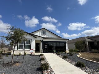 Street view A beautifully designed modern farmhouse-style model home with a white and black color scheme. The landscaping features low-maintenance gravel beds, a concrete walkway, and young trees.