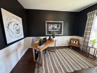 A modern office with dark walls, a sleek wooden desk, abstract art, and stylish furnishings.