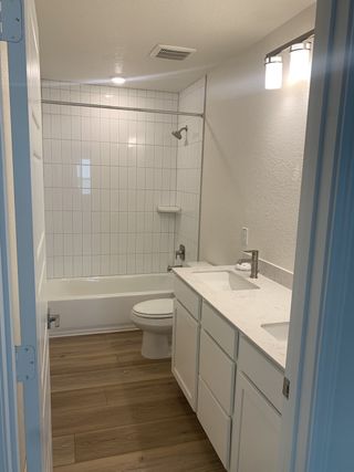 Model Home A stylish bathroom with wood-look flooring, a white vanity, and a tub-shower combo.