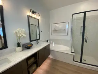 A modern bathroom features a dual vanity with dark wood cabinets and a light quartz countertop, complemented by a black-framed mirror and a glass-enclosed shower.