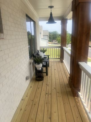 A cozy porch with wood floor, white brick wall, black lighting, and seating with planters for relaxation.
