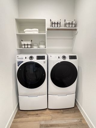 A sleek laundry room featuring state-of-the-art washer and dryer, built-in shelving, and light wood flooring.