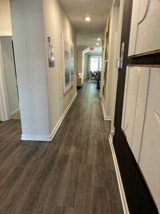A modern hallway with sleek wood flooring, contemporary artwork, and recessed lighting leading to a bright living area.