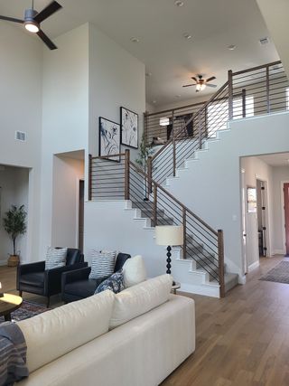 A modern living area featuring a high ceiling, elegant staircase, and cozy seating, enhanced by stylish artwork and lighting.