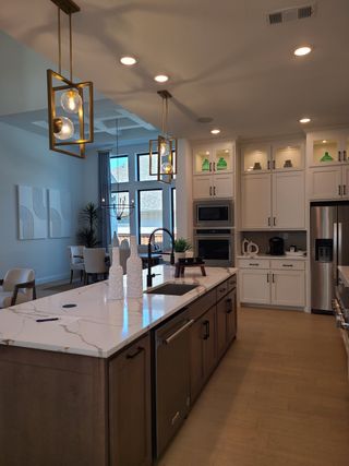 Model Home A modern kitchen featuring a marble island, elegant lighting, and white cabinetry, seamlessly flowing into the dining area.