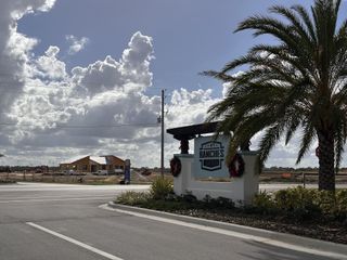The entrance to Ranches at Lake McLeod features a sign with palm trees and a construction site in the background, indicating ongoing development.
