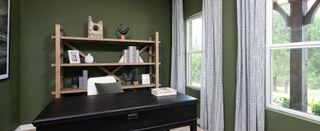 A serene home office with deep green walls, a wooden shelf, and large windows framed by patterned curtains.