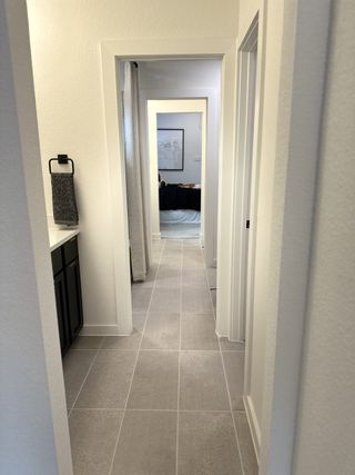 A modern hallway with sleek tile flooring, light walls, and black accents leading into a cozy bedroom.