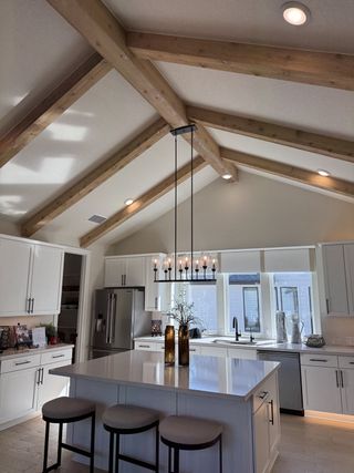 A modern kitchen featuring exposed wood beams, a large island with seating, and sleek white cabinetry.