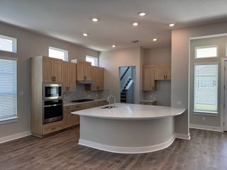 A modern kitchen featuring sleek wood cabinets, stainless steel appliances, and a curved island under ample lighting.