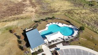 Aerial view of a sparkling pool with shaded seating in The Colony- Pine Cove by Sitterle Homes (Bastrop, TX).