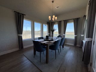 A bright dining room with large windows, elegant drapes, a sleek table, and stylish blue chairs.