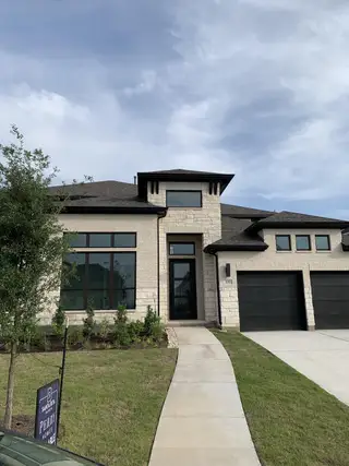Street view A modern stone two-story home with dark accents in Santa Rita Ranch by Perry Homes (Liberty Hill, TX).