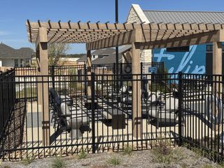 A charming outdoor seating area with a wooden pergola and modern fence in Nolina 60' by Perry Homes (Georgetown, TX).