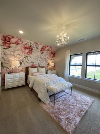 A cozy bedroom with floral wallpaper, elegant chandelier, and plush pink accents for a serene atmosphere.